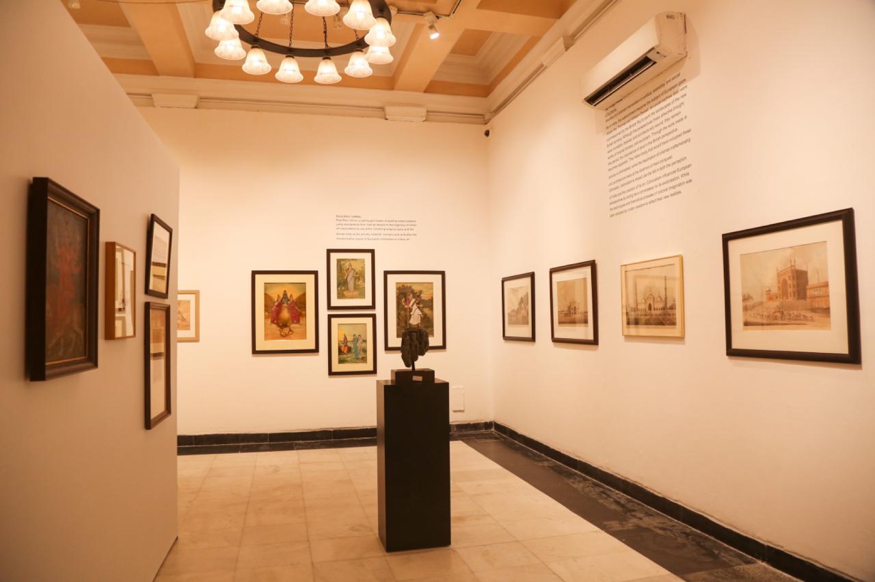 The Raja Ravi Varma room: oleographs and a bronze on a dark plinth under a chandelier.